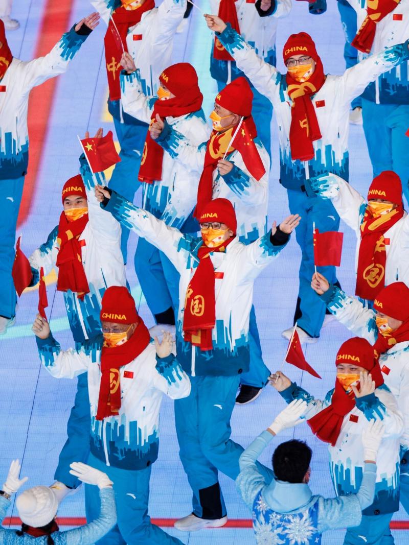 About 20 people march in the main stadium of the Beijing 2022 Games while waving small Chinese flags.